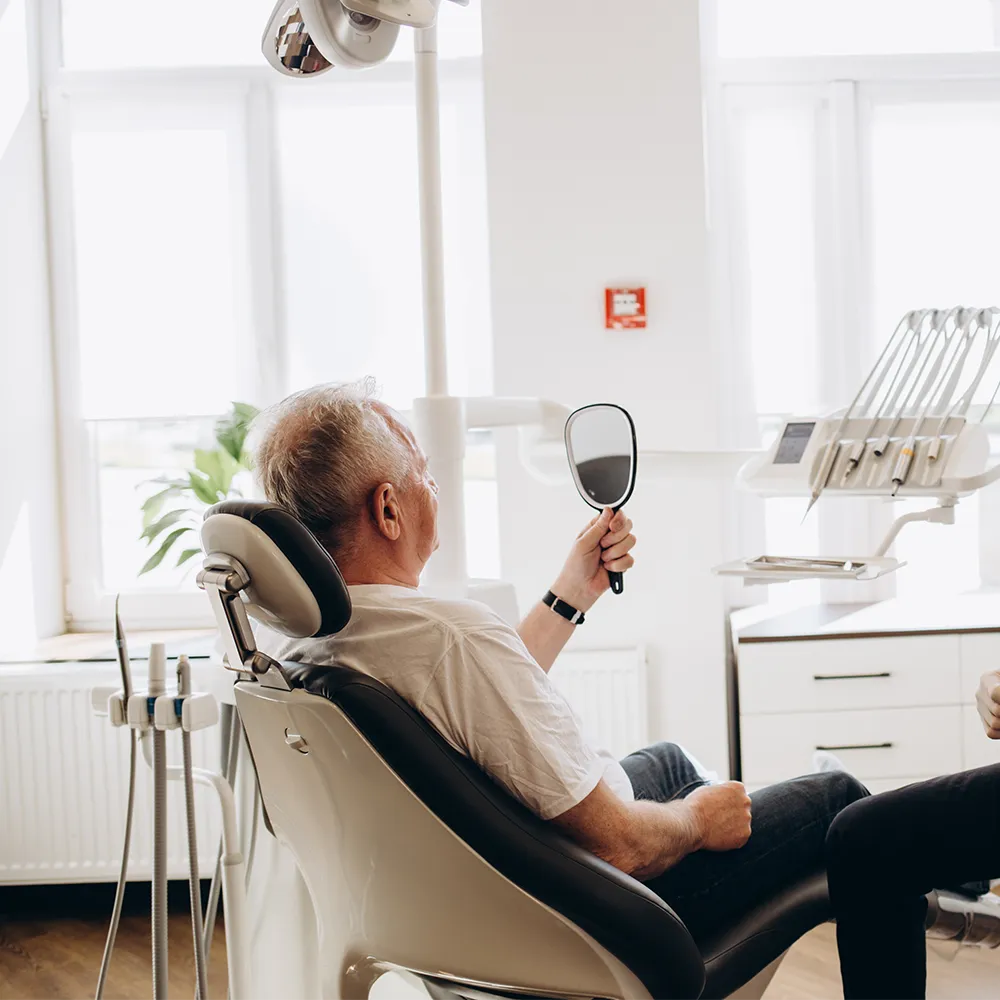 older man in dentist chair with handheld mirror